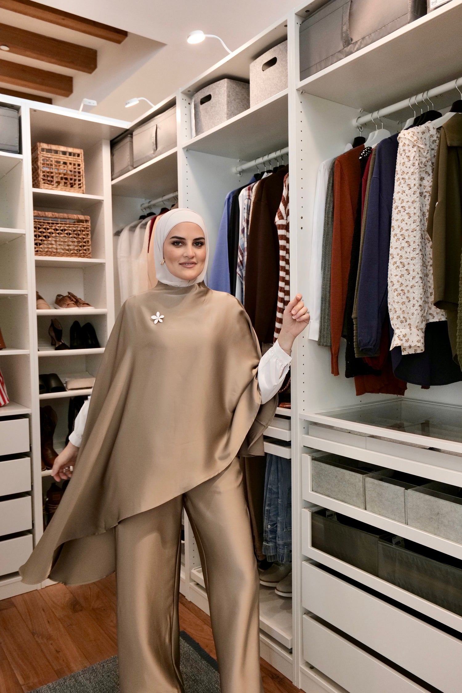 Woman in a beige outfit standing in a well-organized closet with clothes and shelves.